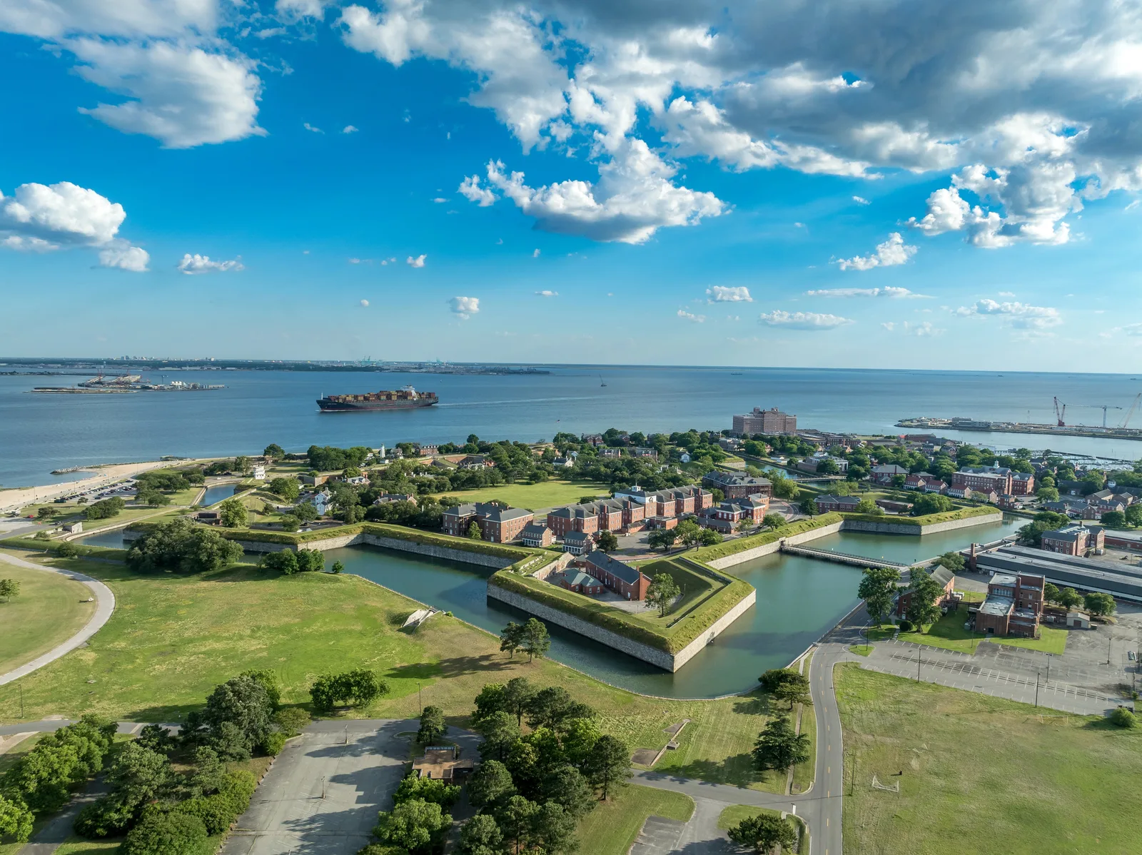Aerial view of a historic star-shaped coastal fort and a cargo ship navigating the Hampton Roads waterway.